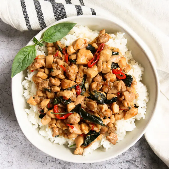 an overhead shot of a bowl of thai basil chicken over rice with a sprig of thai basil