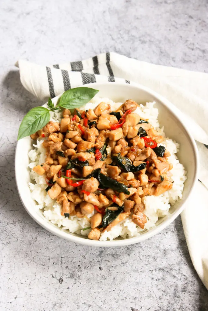 a bowl of thai basil chicken over rice with a sprig of thai basil