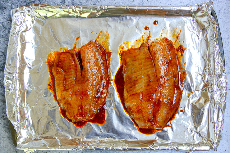 two seasoned tilapia filets on an aluminum wrapped cookie sheet