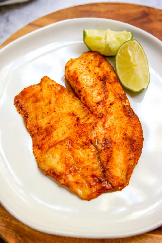 a close up of a seasoned filet of tilapia with a lime