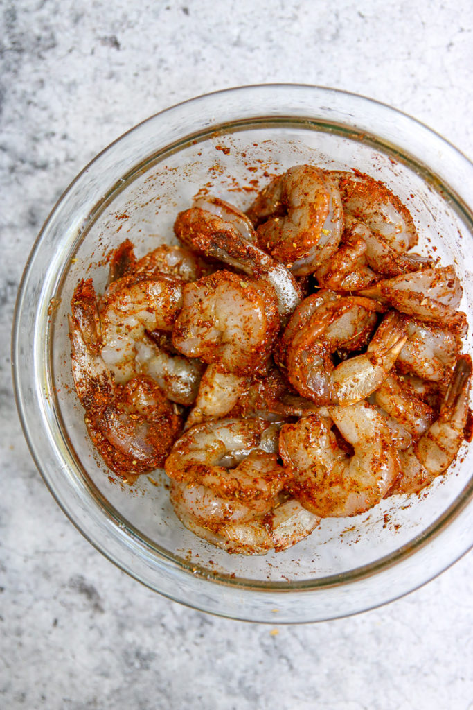 a glass bowl of seasoned peeled, raw shrimp