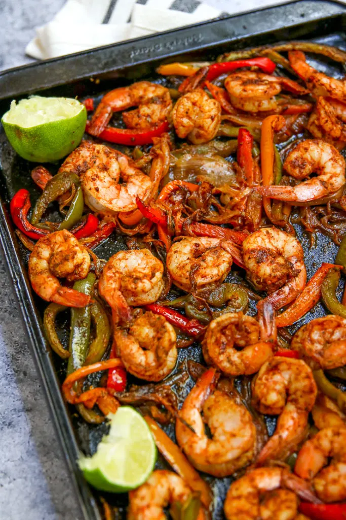 a close up of seasoned cooked shrimp, onions and peppers with lime wedges