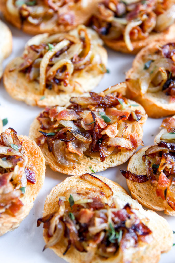 a close up of crostini on a plate topped with bacon, caramelized onion, thyme, and balsamic glaze