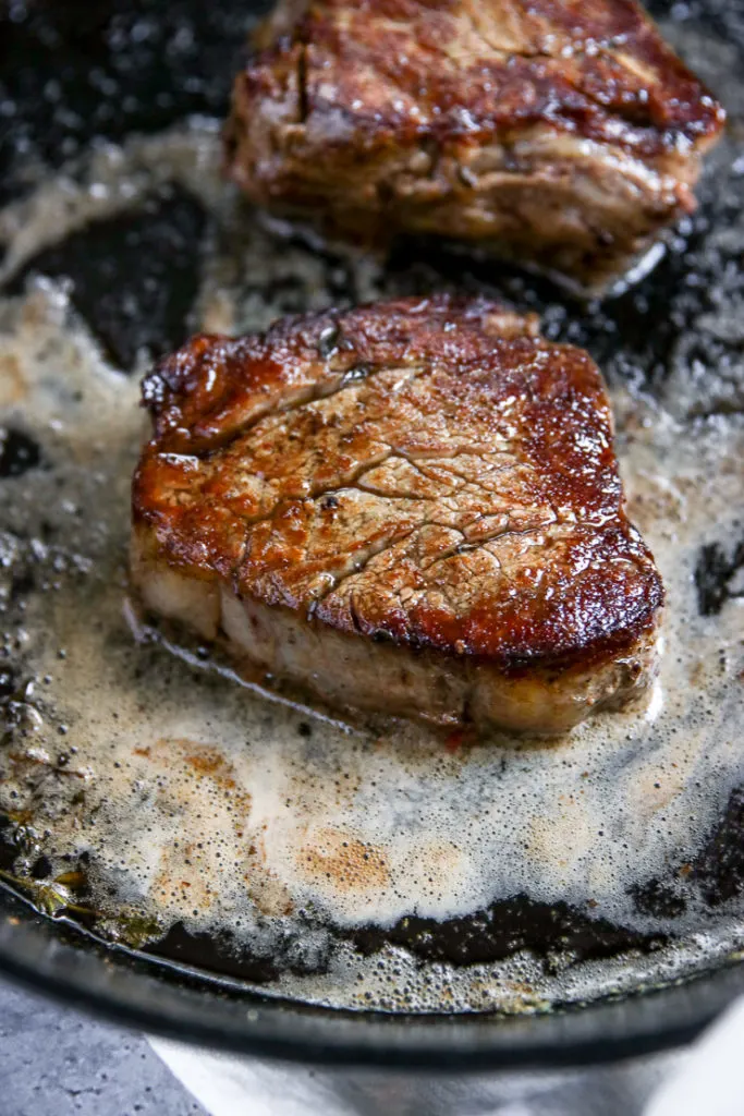 a close up of a seared filet mignon in melted butter on a cast iron