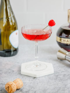 a coupe glass of red chambord and champagne with a champagne bottle and chambord bottle