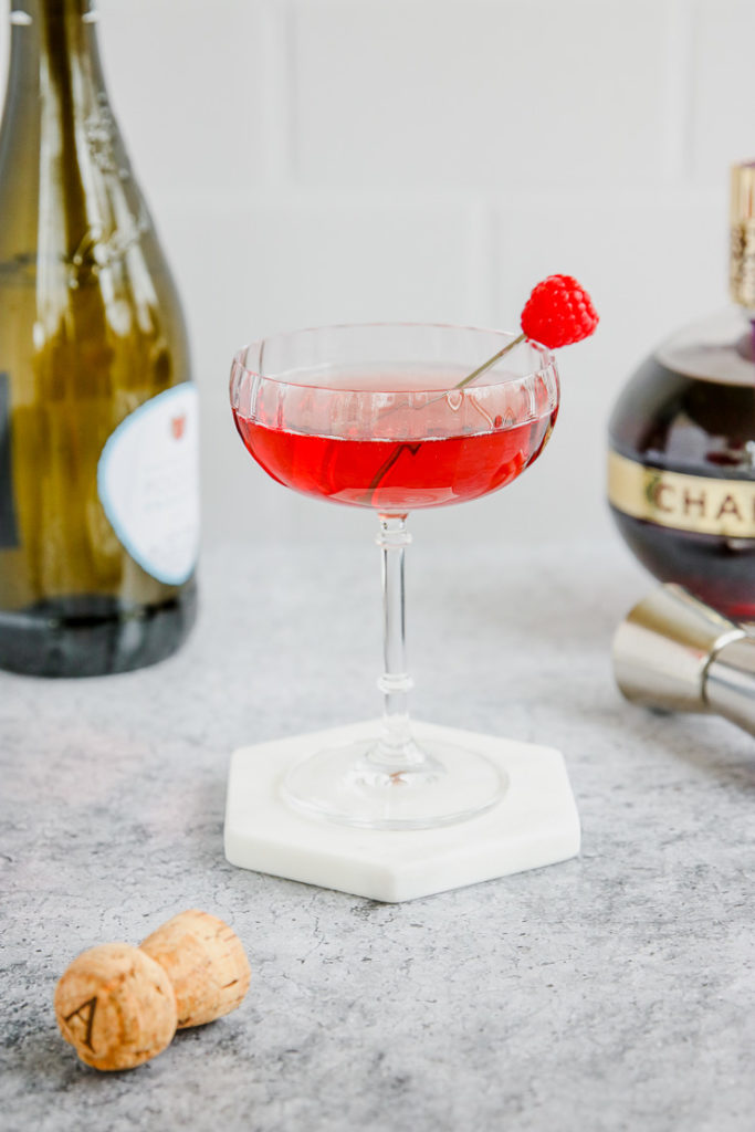 a coupe glass of red chambord and champagne with a champagne bottle and chambord bottle