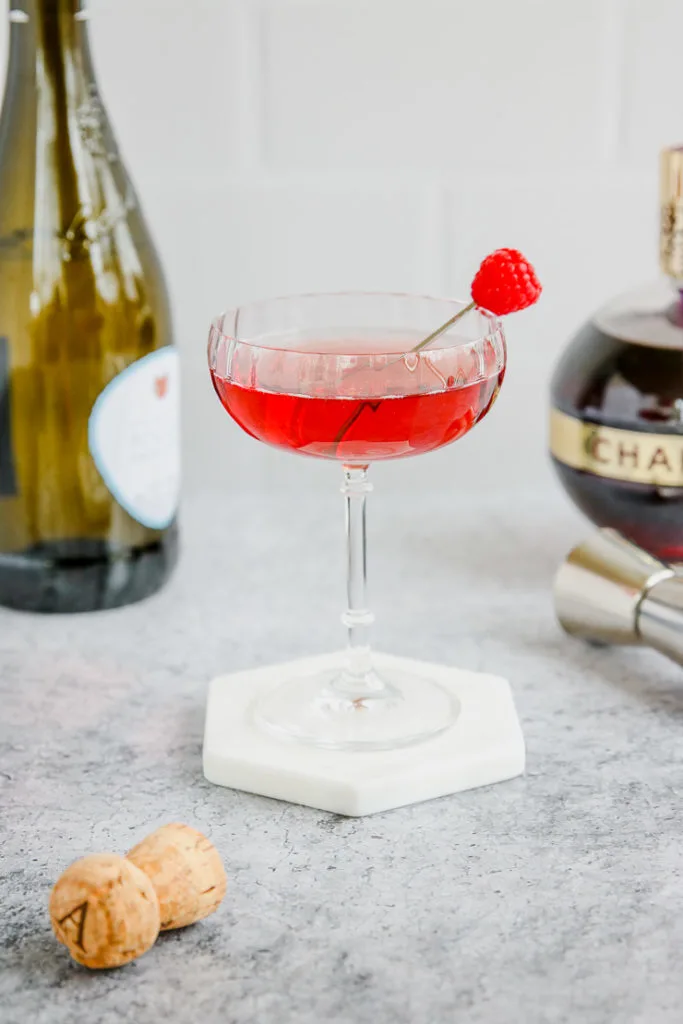 a coupe glass of red chambord and champagne with a champagne bottle and chambord bottle