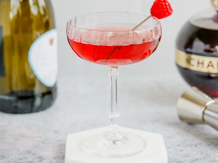 a coupe glass of red chambord and champagne with a champagne bottle and chambord bottle