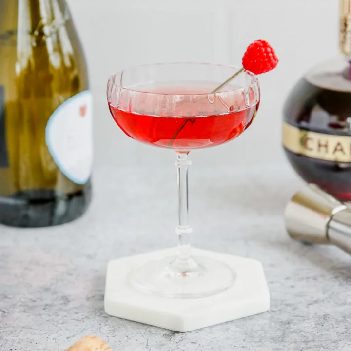 a coupe glass of red chambord and champagne with a champagne bottle and chambord bottle