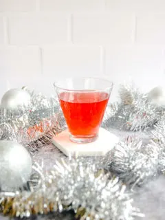 a stemless martini glass with cranberry ginger ale punch surrounded by silver garland and baubles