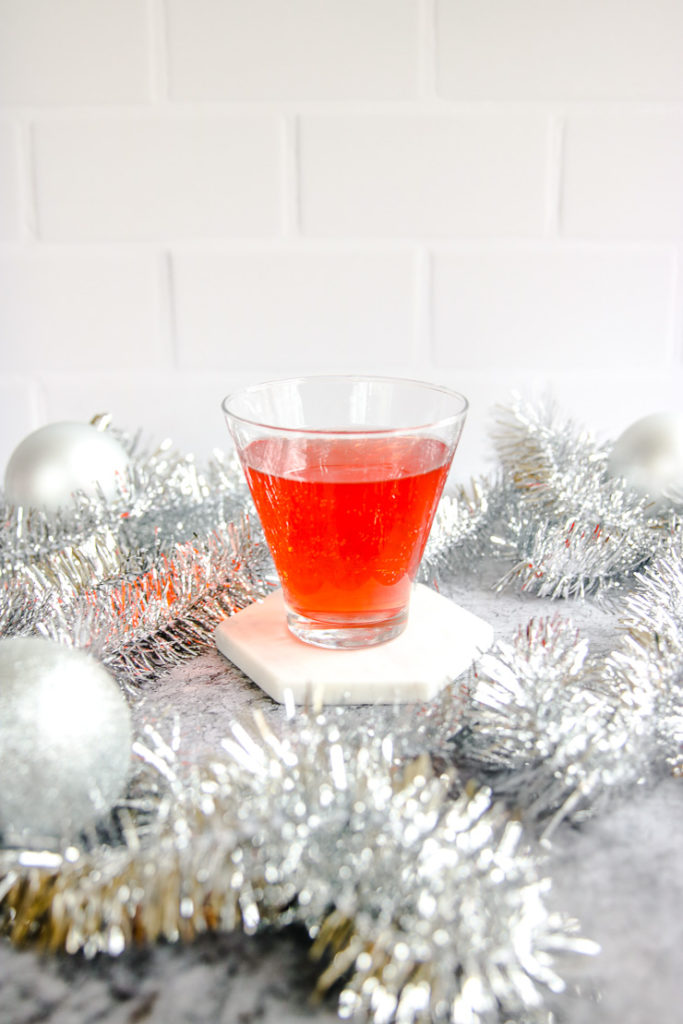 a stemless martini glass with cranberry ginger ale punch surrounded by silver garland and baubles