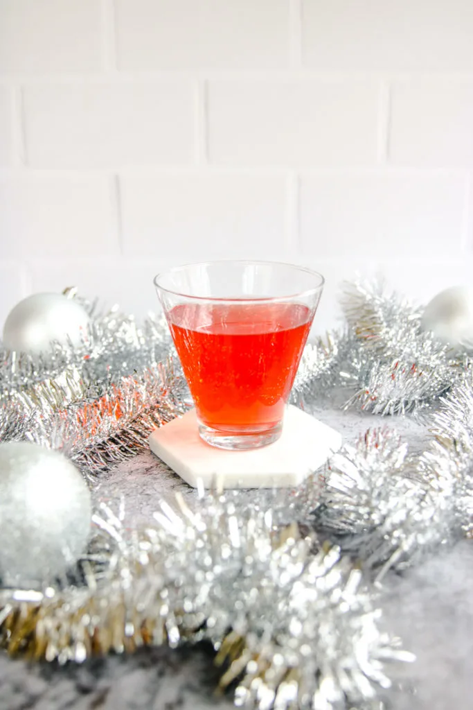 a stemless martini glass with cranberry ginger ale punch surrounded by silver garland and baubles