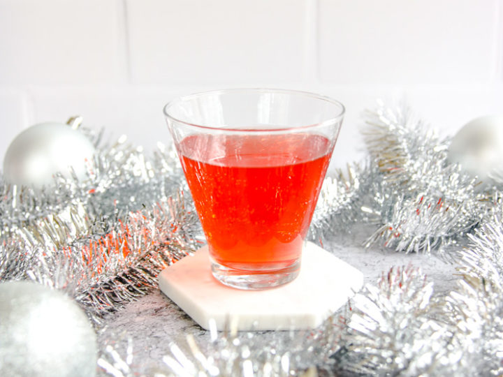 a stemless martini glass with cranberry ginger ale punch surrounded by silver garland and baubles