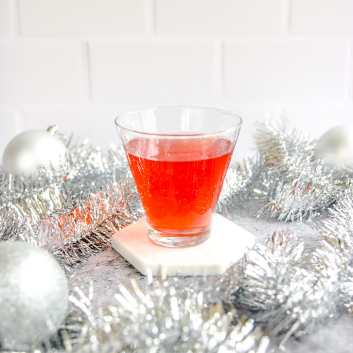 a stemless martini glass with cranberry ginger ale punch surrounded by silver garland and baubles