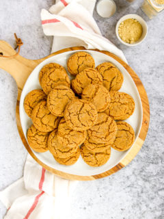 a white plate of ginger snaps on a wood platter next to a napkin