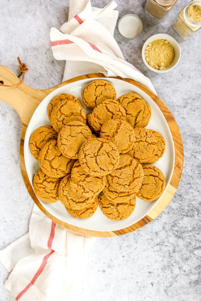 a white plate of ginger snaps on a wood platter next to a napkin