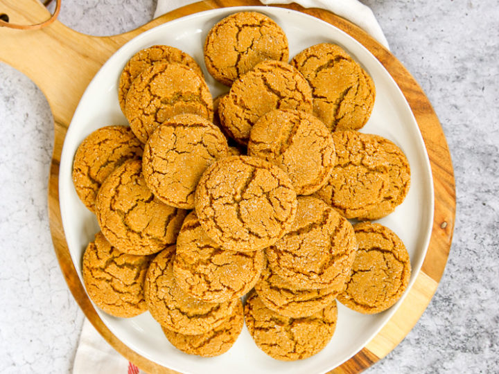 a white plate of ginger snaps on a wood platter next to a napkin