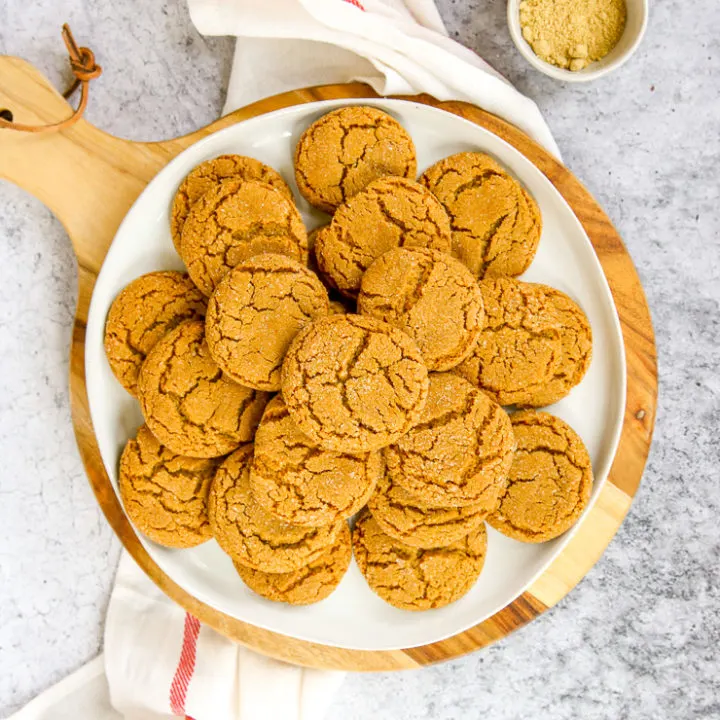 a white plate of ginger snaps on a wood platter next to a napkin