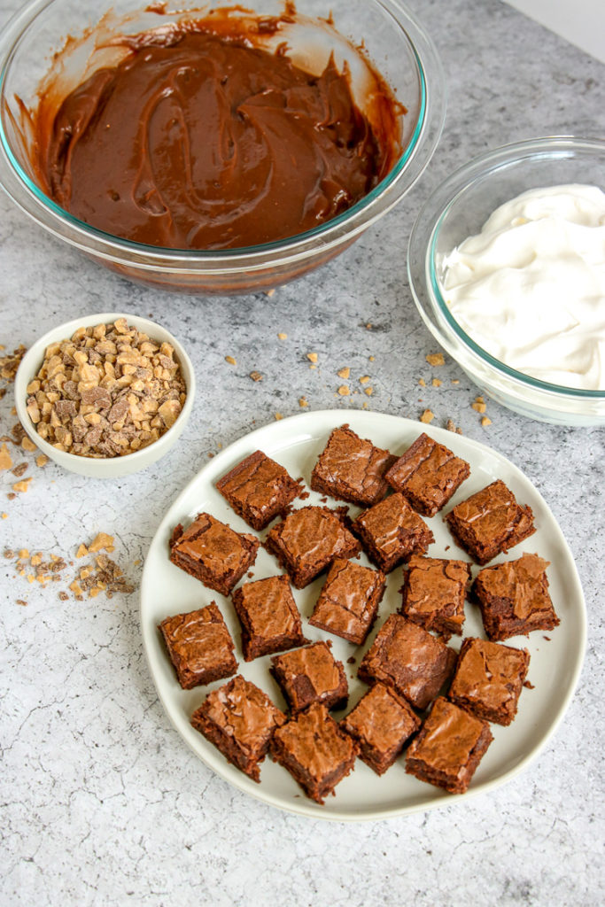 a plate of brownies, bowls of chocolate pudding and cool whip, and a bowl of heath crumbles