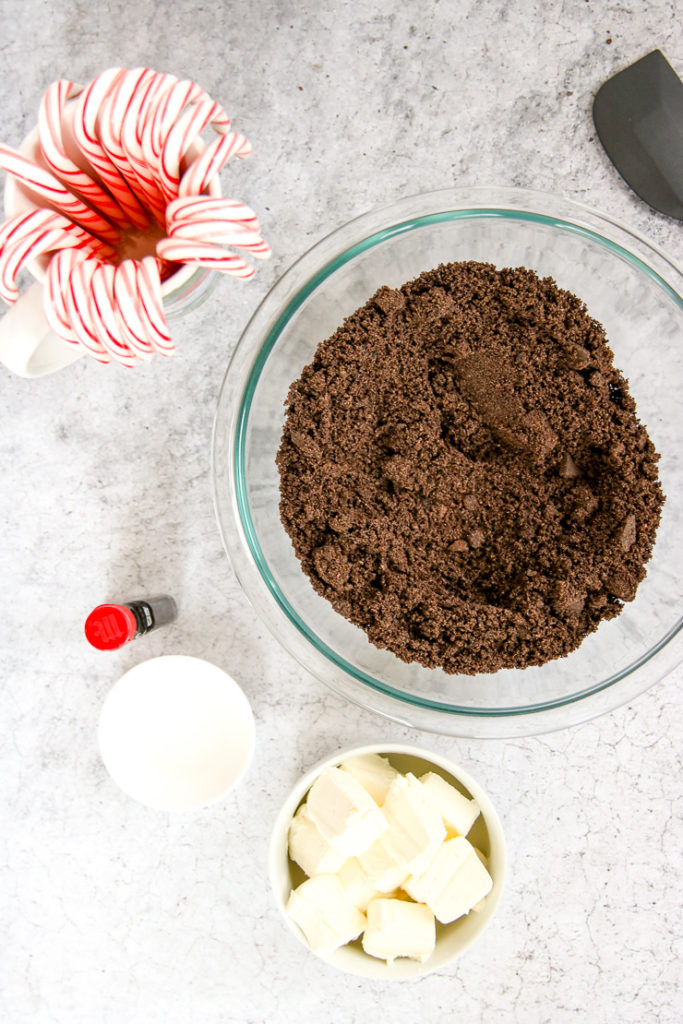 a bowl of crushed oreos, candy canes, a bowl of sliced cream cheese, and peppermint extract