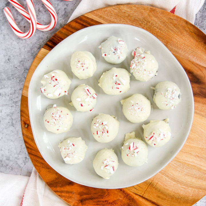 a plate of peppermint oreo truffles on a wooden platter next to candy canes