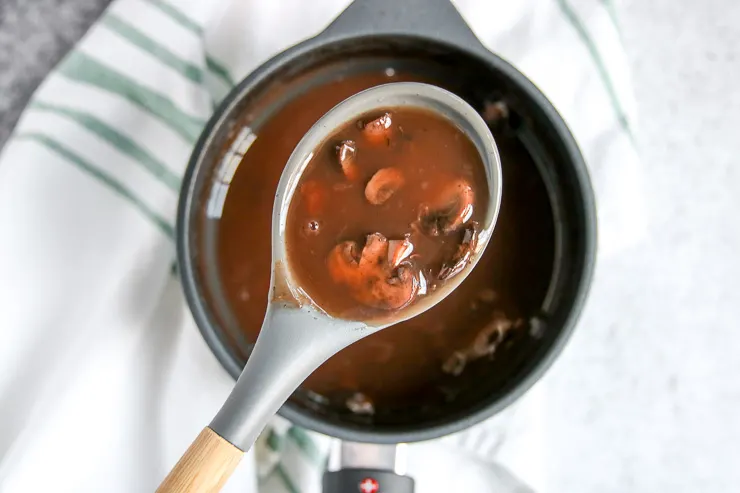 a spoon of red wine mushrooms over a saucepot