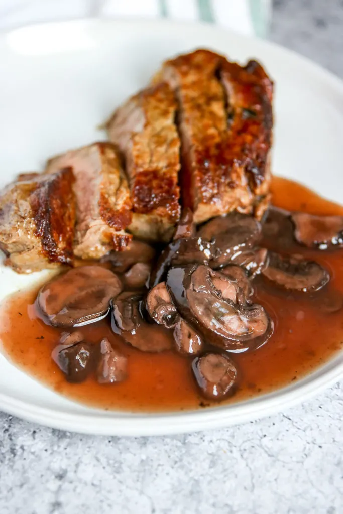 a close up of red wine mushrooms on a plate with a sliced steak