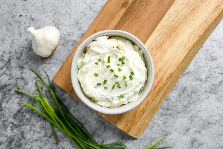 a bowl of roasted garlic spread on a wooden platter