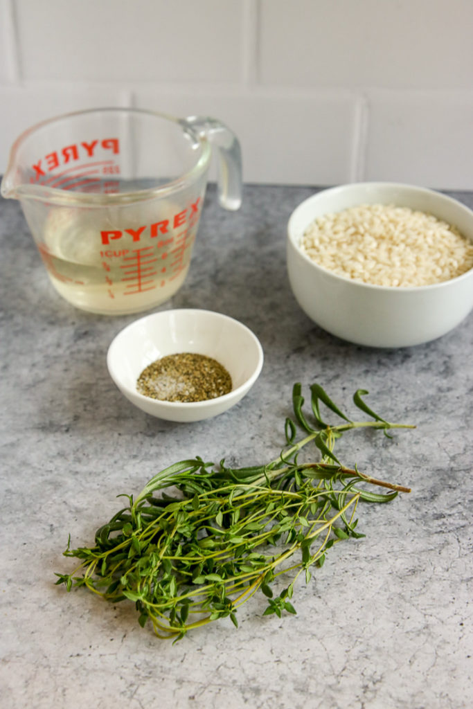 fresh thyme and rosemary, a bowl of salt and pepper, arborio rice, and a glass measuring cup full of white wine