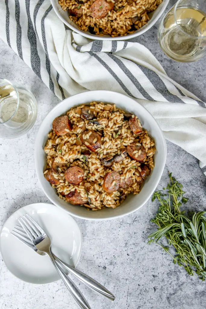 an overhead shot of two bowls of sausage mushroom risotto and two wine glasses