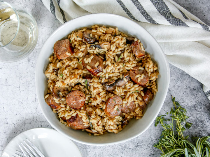 an overhead shot of two bowls of sausage mushroom risotto and two wine glasses