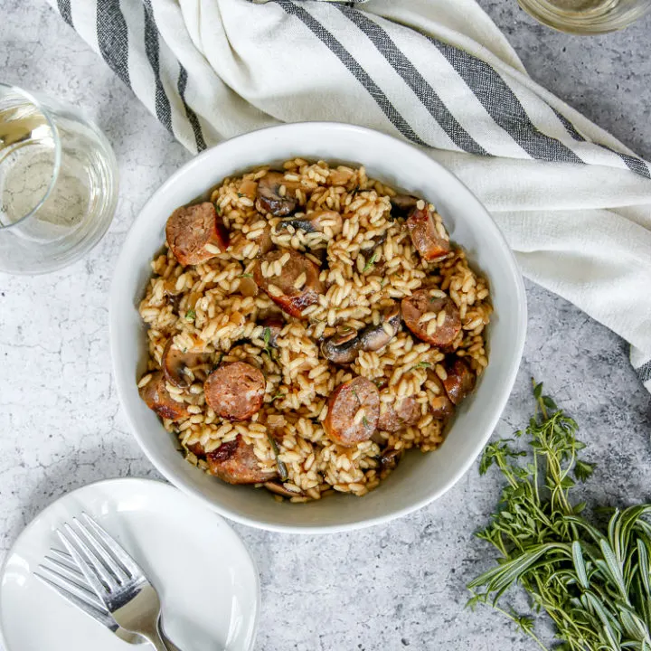 an overhead shot of two bowls of sausage mushroom risotto and two wine glasses