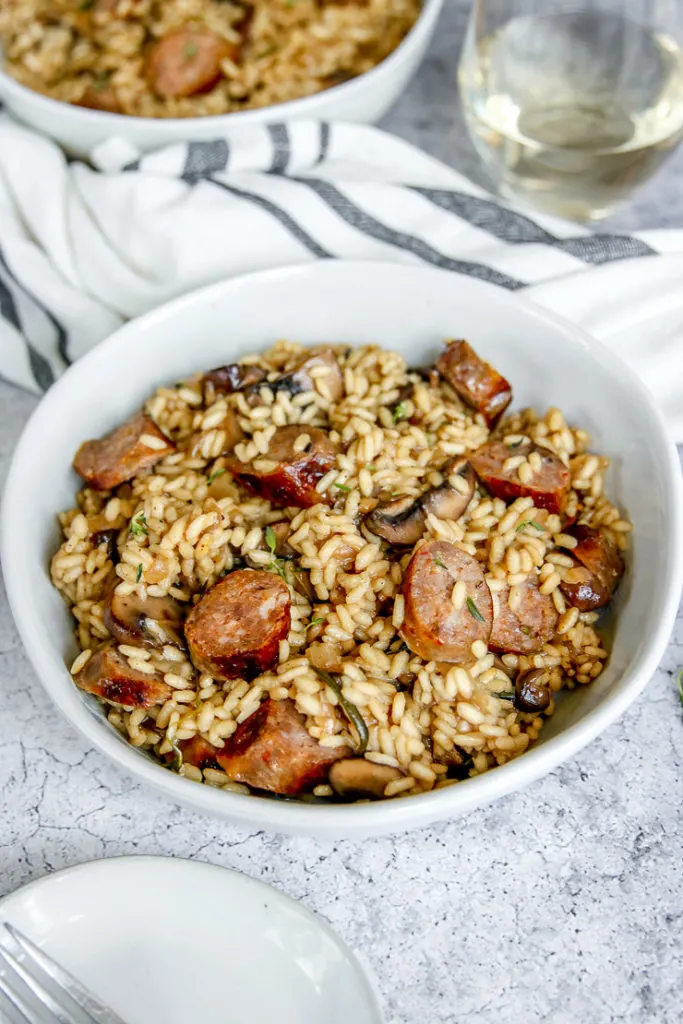 a close up of white bowl of sausage mushroom risotto