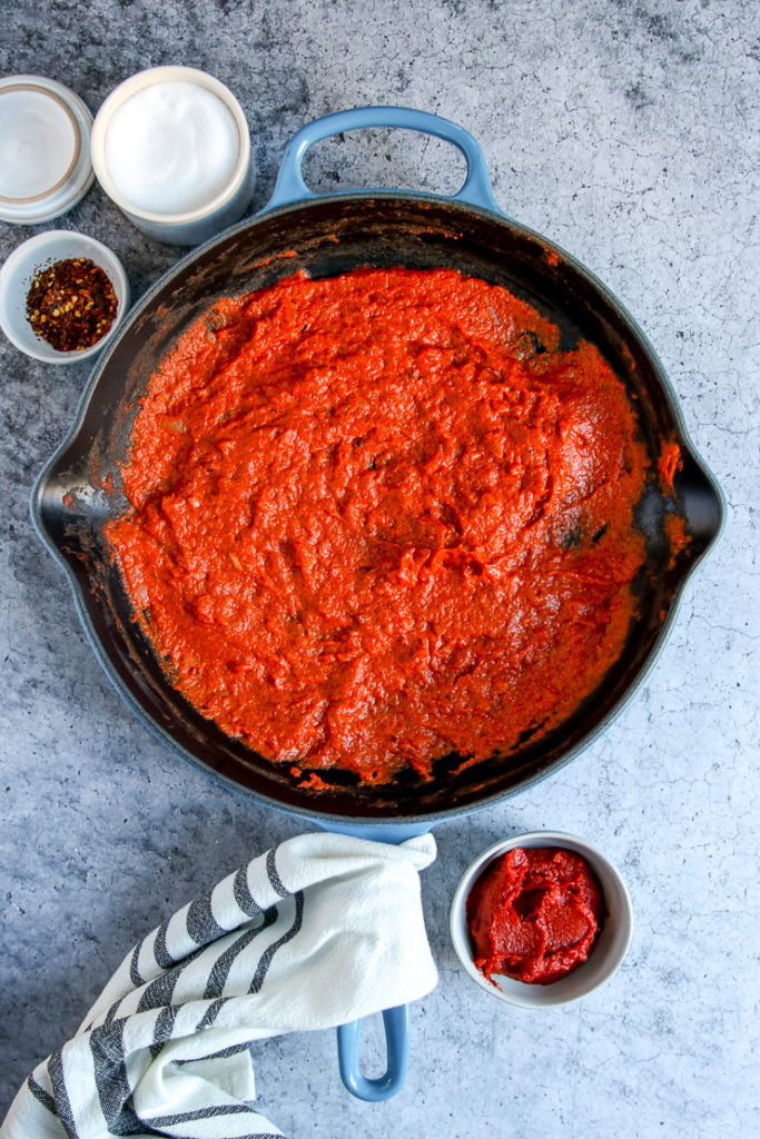 a skillet filled with vodka sauce and bowls of red pepper flakes, salt, and tomato paste