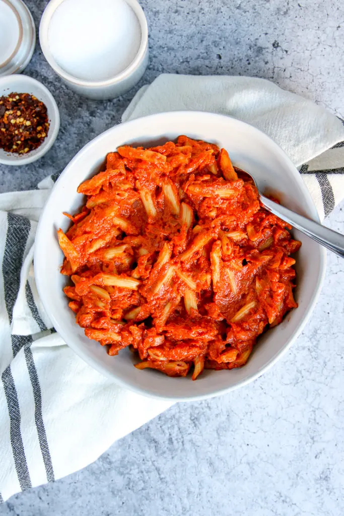 an overhead shot of penne alla vodka on a napkin with salt and red pepper flakes