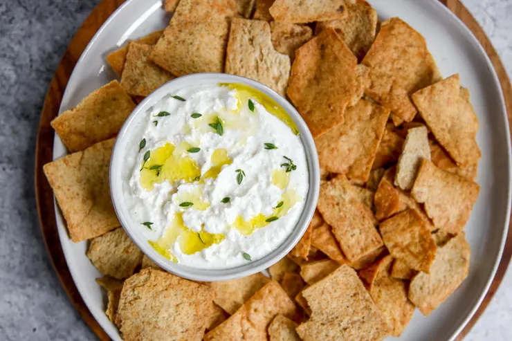 an overhead shot of whipped feta in a white bowl on a plate of pita chips