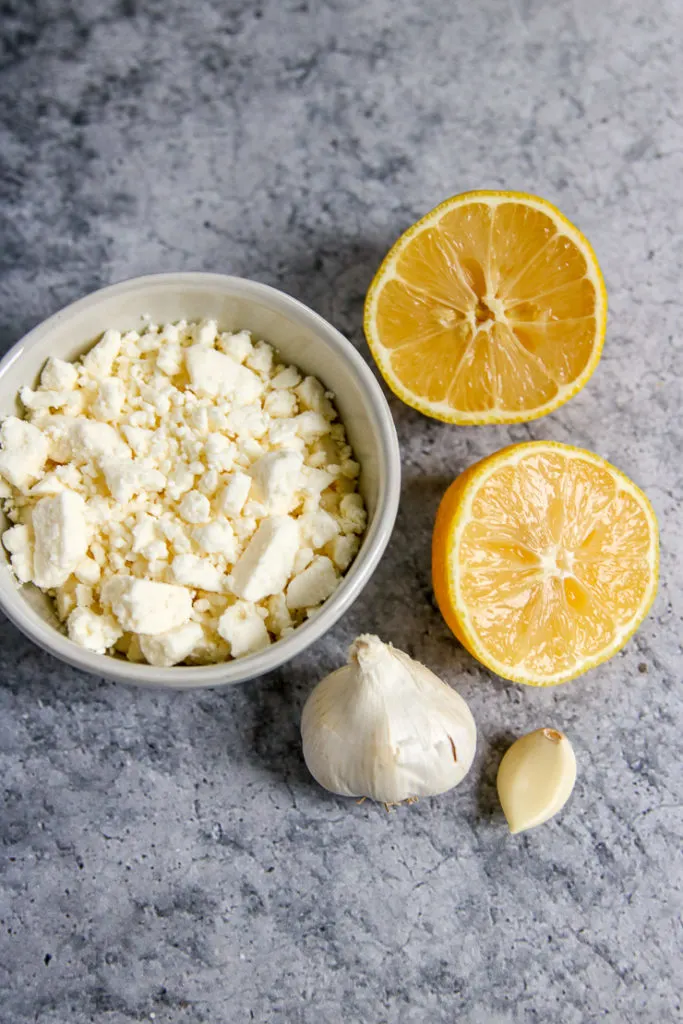 a bowl of crumbled feta, halved lemon, head of garlic and a garlic clove