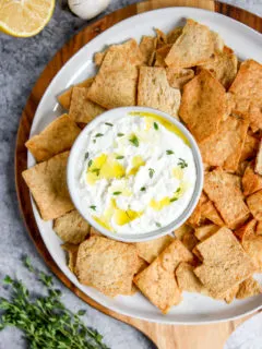 a bowl of whipped feta dip sitting on a plate with pita chips