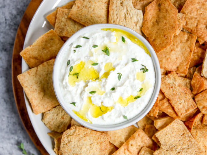 a bowl of whipped feta dip sitting on a plate with pita chips