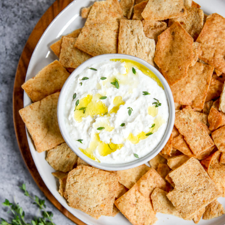 a bowl of whipped feta dip sitting on a plate with pita chips