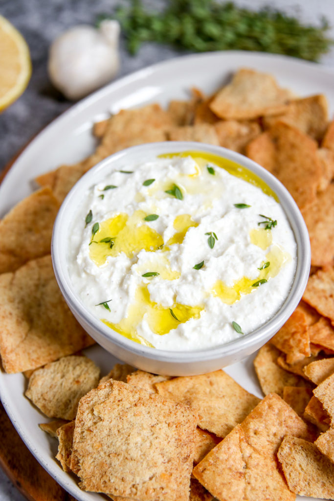 a close up of whipped feta dip drizzled in olive oil and fresh thyme