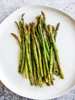 a white plate full of asparagus right from the air fryer