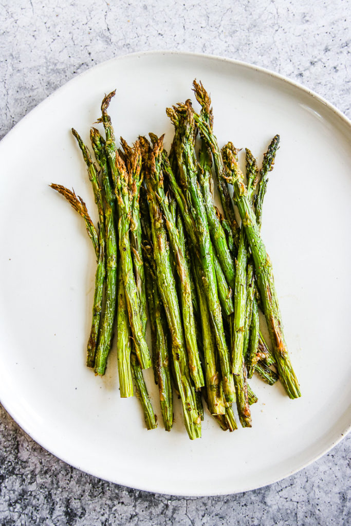 a white plate full of asparagus right from the air fryer