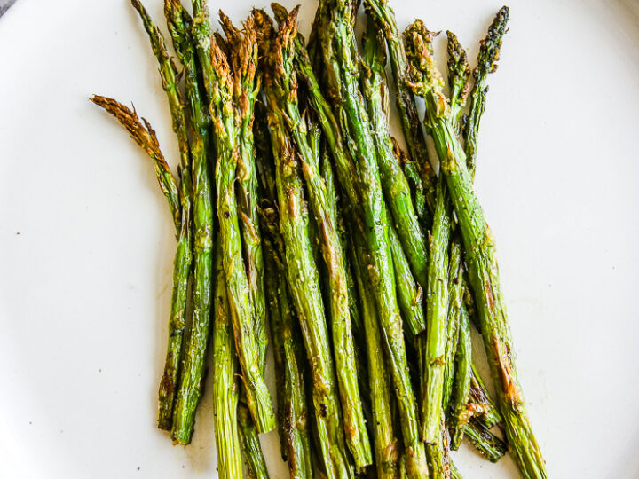 a white plate full of asparagus right from the air fryer