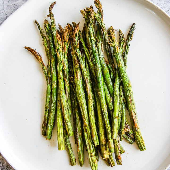 a white plate full of asparagus right from the air fryer