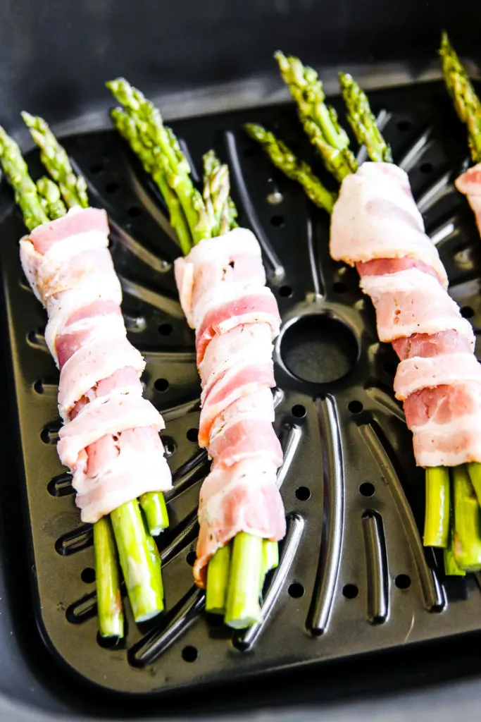 raw bacon wrapped around four asparagus stalks in the air fryer basket