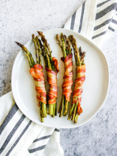 a plate of air fryer bacon wrapped asparagus on a grey and white napkin