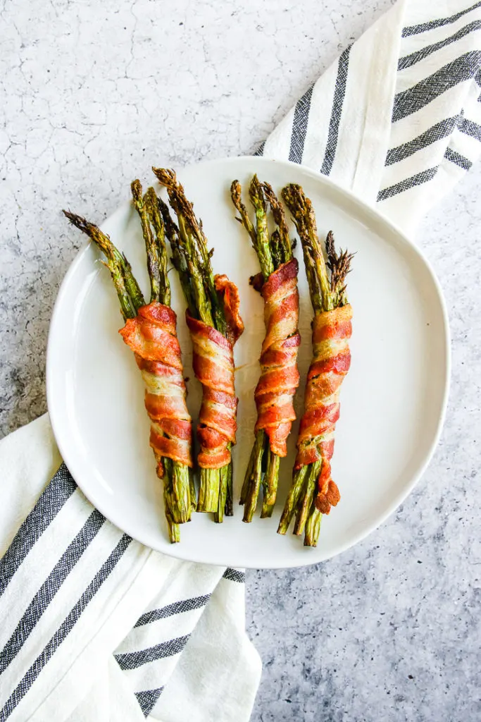 a plate of air fryer bacon wrapped asparagus on a grey and white napkin