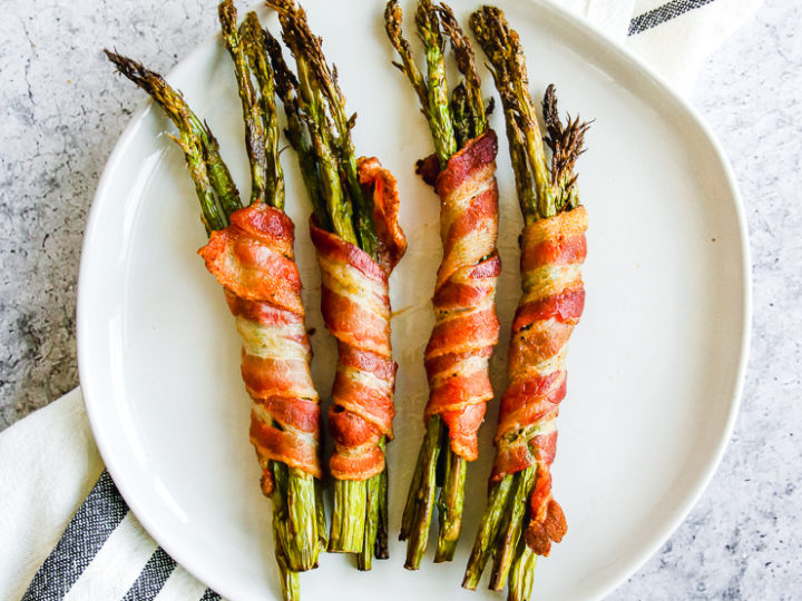 a plate of air fryer bacon wrapped asparagus on a grey and white napkin