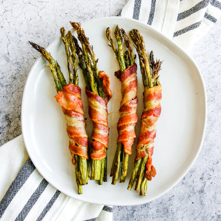 a plate of air fryer bacon wrapped asparagus on a grey and white napkin